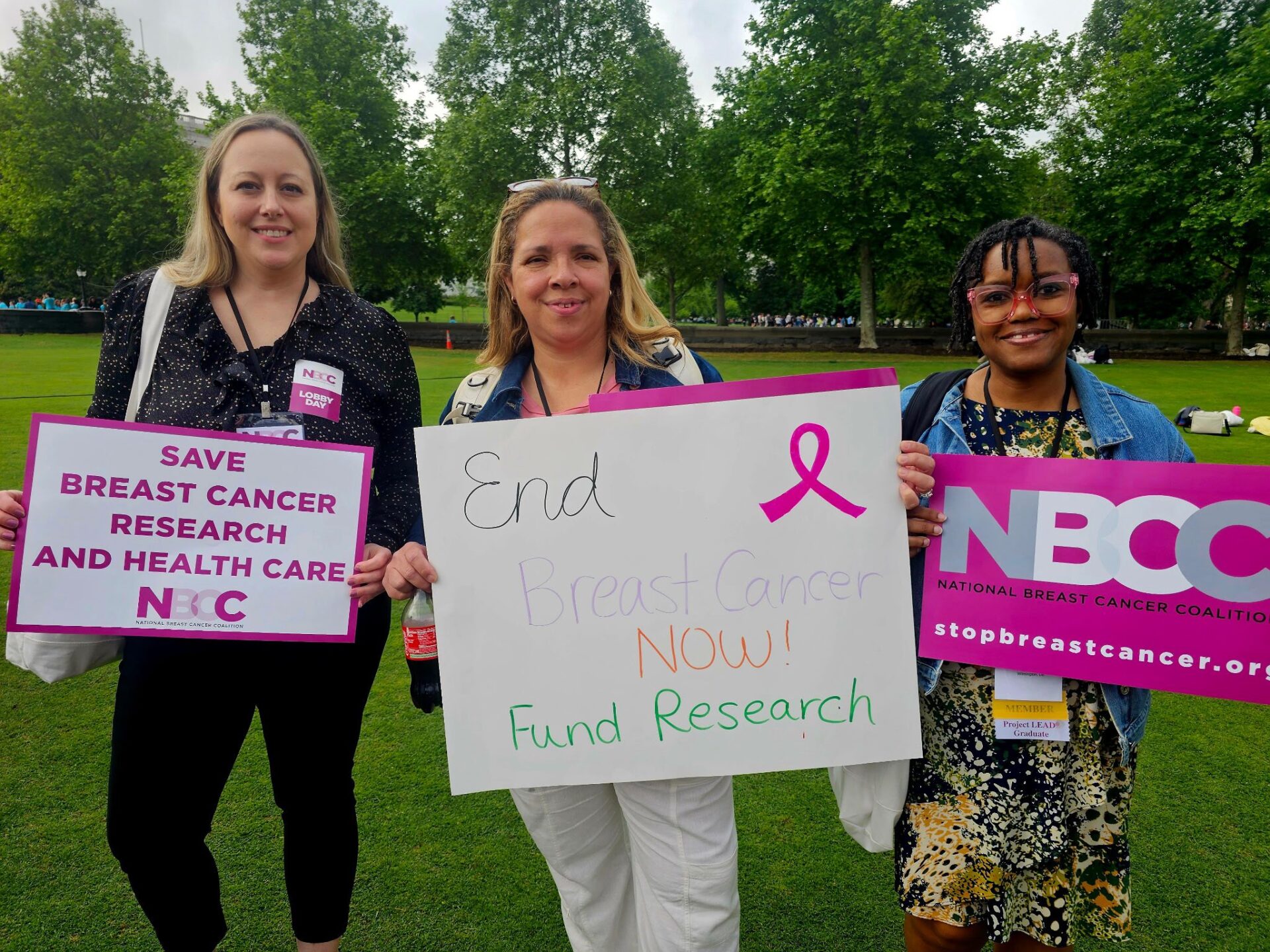 three women holding advocacy signs in Washington DC featuring wording such as "end breast cancer now! fund research".
